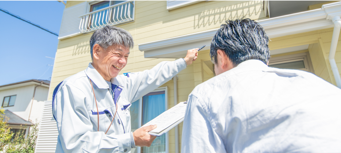 外壁の前で作業員が住人に説明をしながら住宅の外装を指差している場面