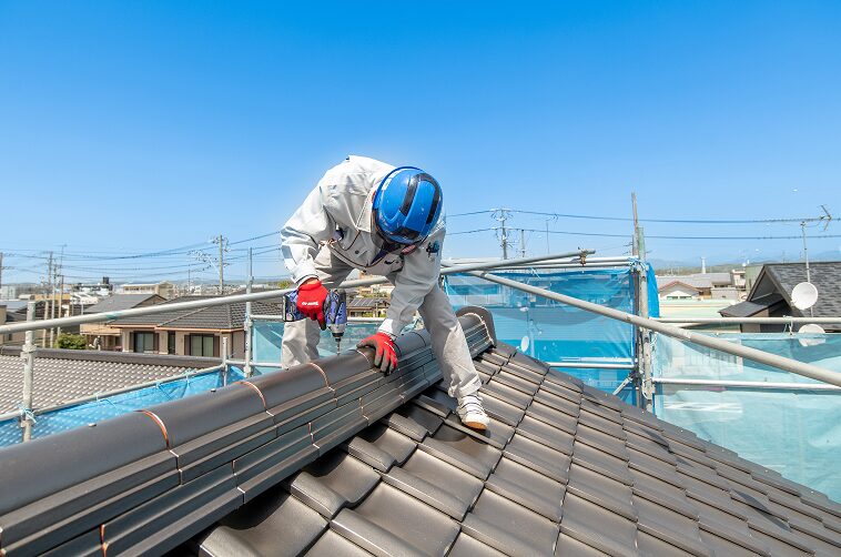 瓦屋根の棟部分を電動ドライバーで補修中の作業員