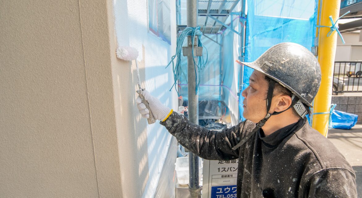 作業員が外壁に白い塗料をローラーで丁寧に塗装している様子