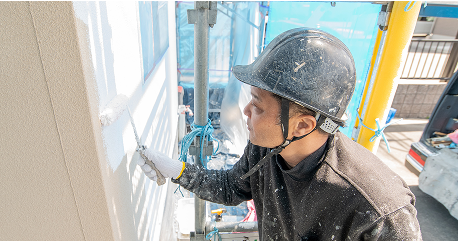 作業員が建物の外壁に白い塗料をローラーで塗装している様子